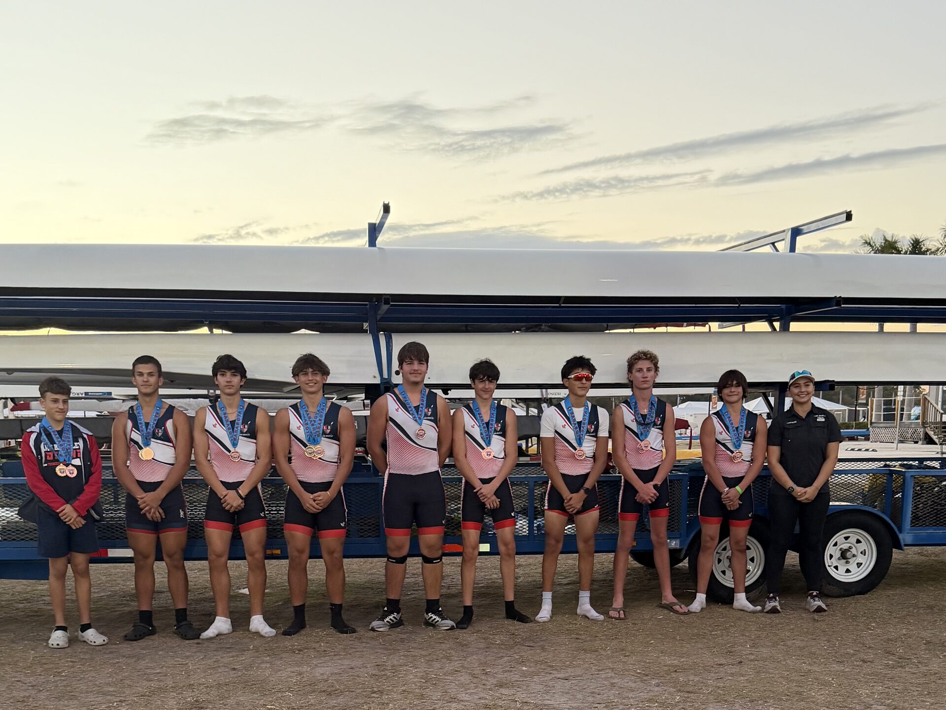 Boys 8+ crew with medals after racing, sunset behind the trailer